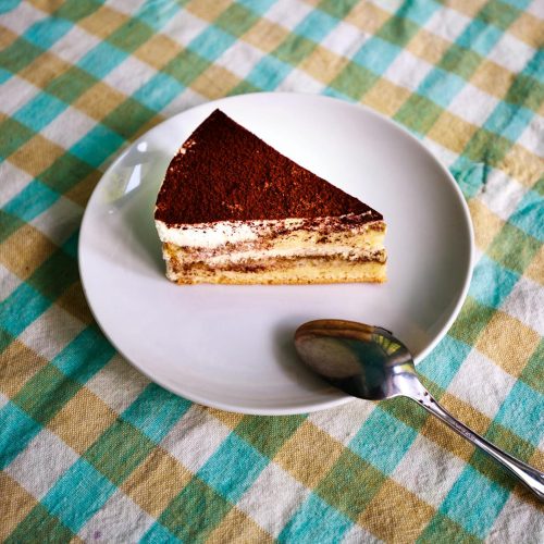 Slice of classic tiramisu on a white plate dusted with cocoa powder