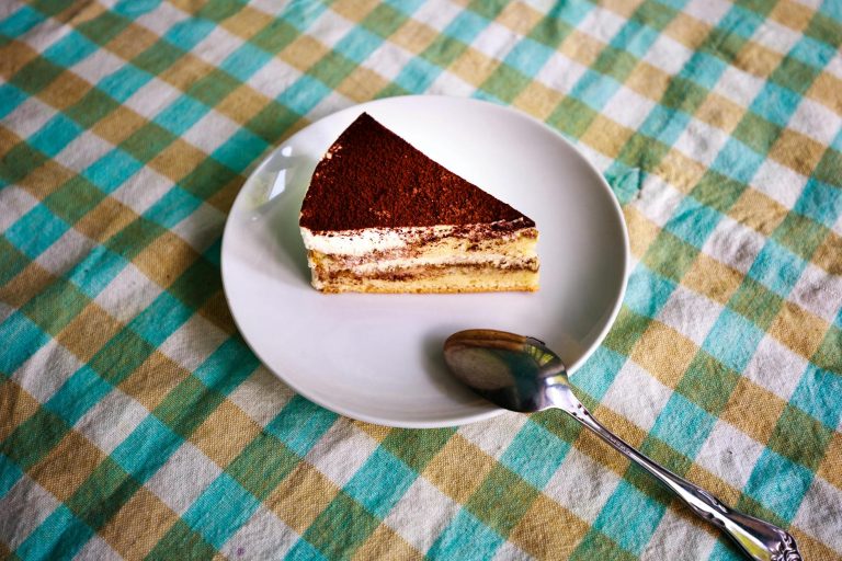 Slice of classic tiramisu on a white plate dusted with cocoa powder