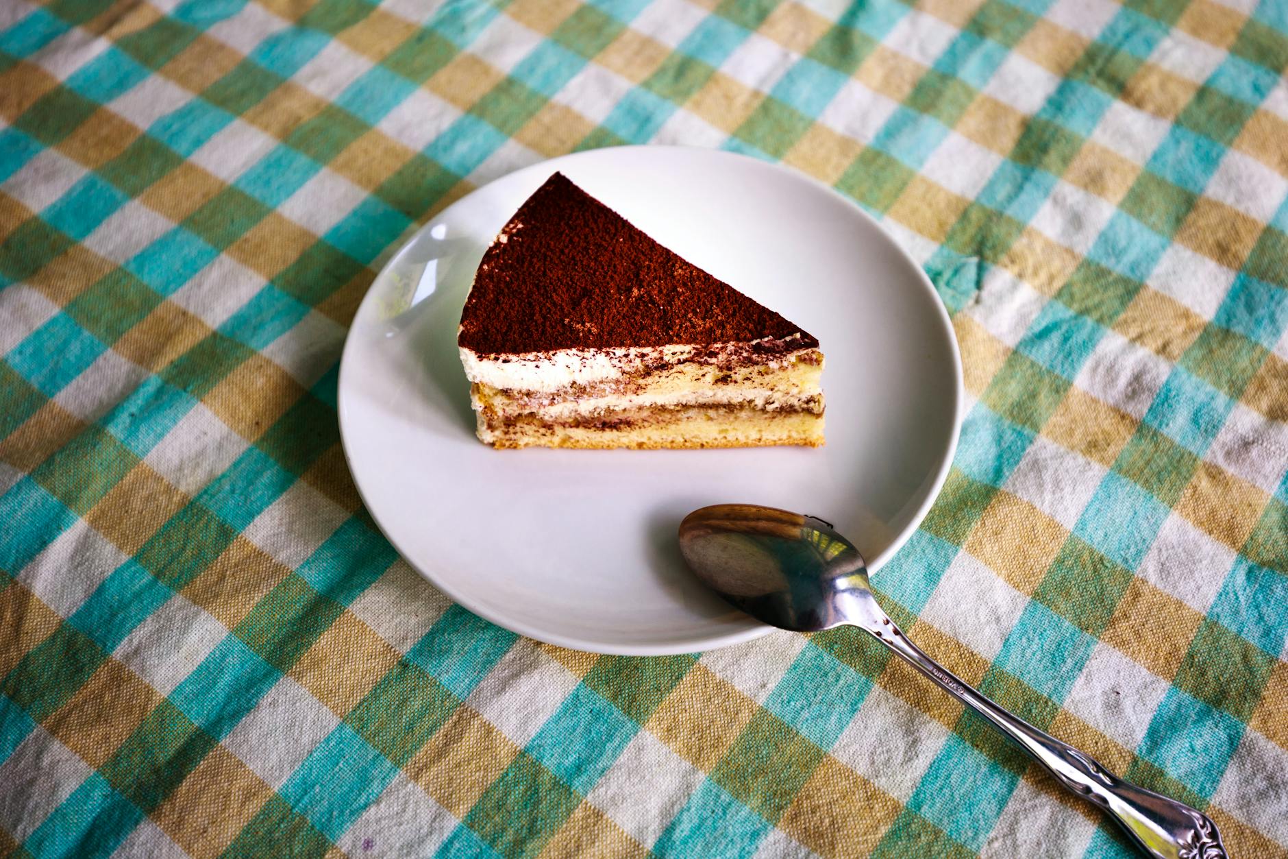 Slice of classic tiramisu on a white plate dusted with cocoa powder