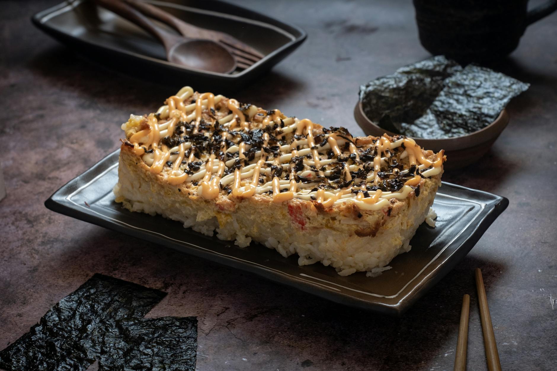 baked fusion sushi casserole topped with avocado, cucumber, and spicy mayo in a white dish