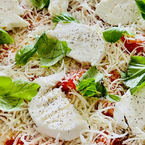 Unbaked homemade margherita pizza topped with mozzarella and basil