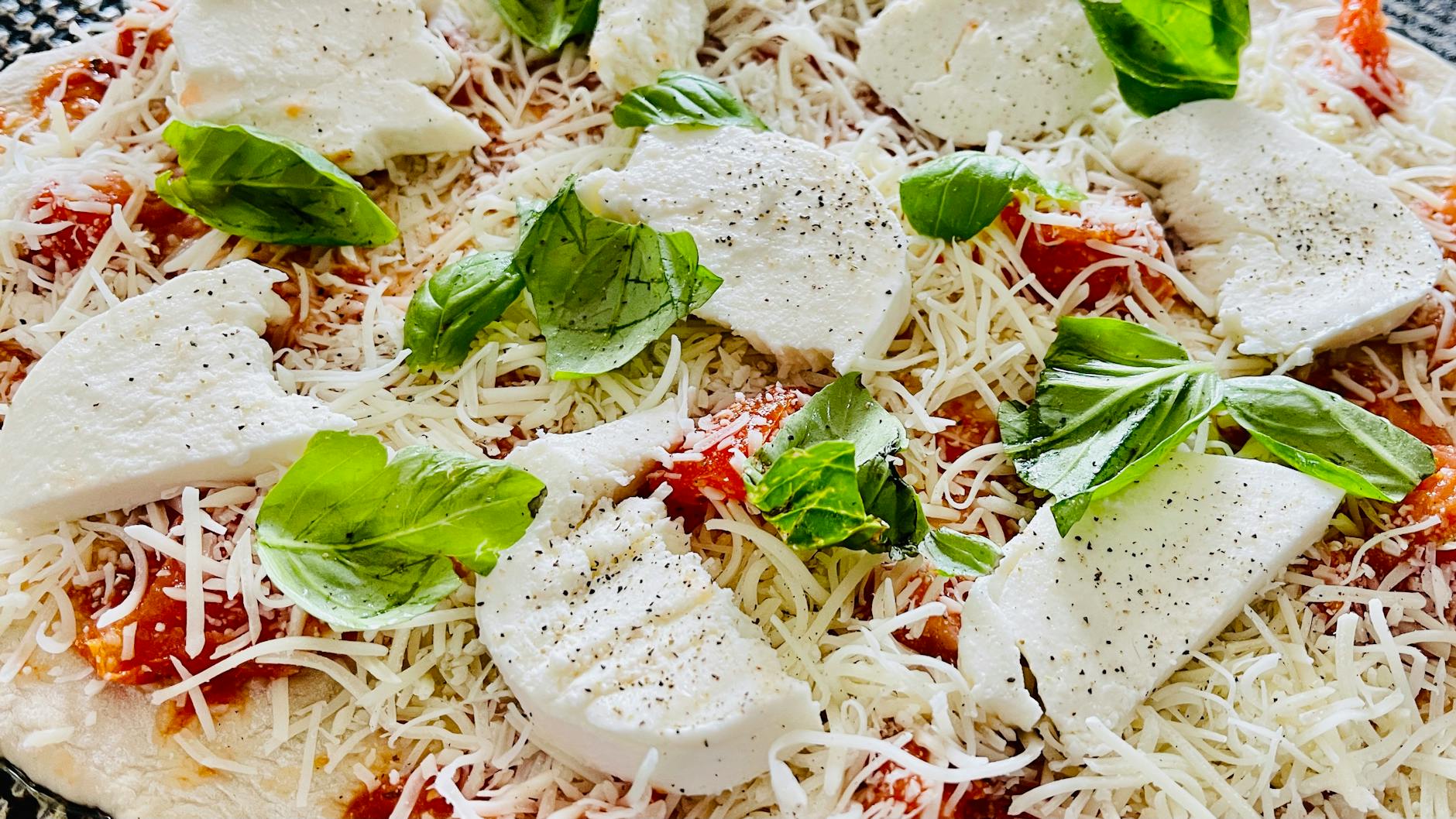 Overhead view of homemade margherita pizza with bubbly crust, melted mozzarella, and fresh basil on a wooden board