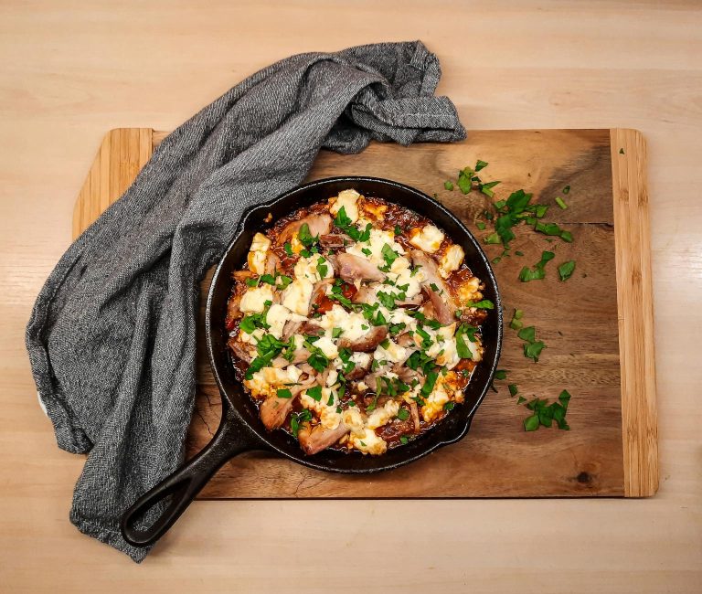 Skillet of hot honey feta chicken thighs topped with crumbled feta and herbs