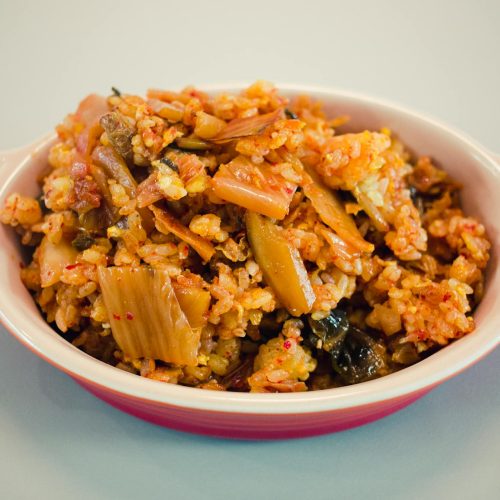 Kimchi and black garlic fried rice in a red dish with scallions