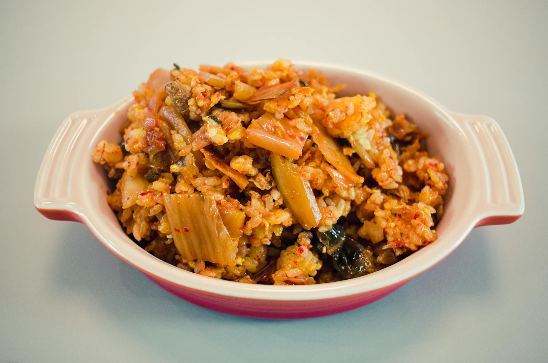Bowl of kimchi and black garlic fried rice topped with egg, sesame seeds, and scallions