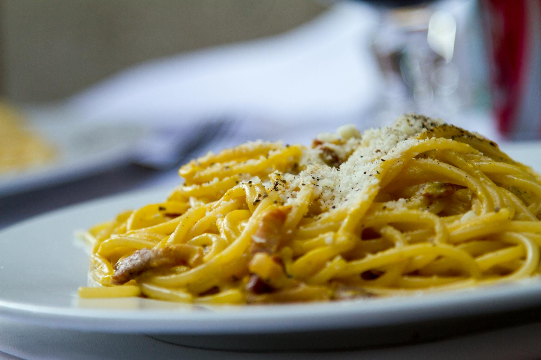Authentic Italian carbonara with spaghetti, guanciale, Pecorino Romano, and black pepper on a white plate