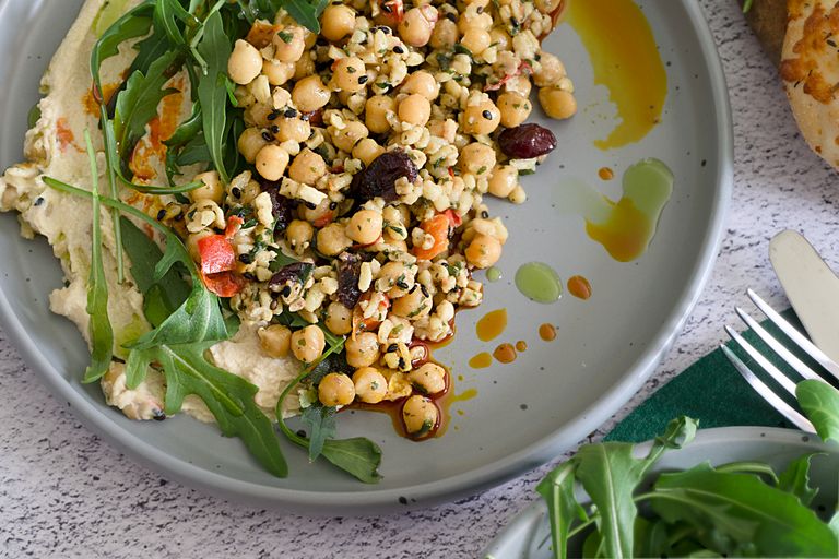 Delicious Mediterranean salad with chickpeas, hummus, arugula, and olives, drizzled with olive oil.