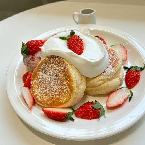 Stack of fluffy Japanese souffle pancakes topped with berries and whipped cream