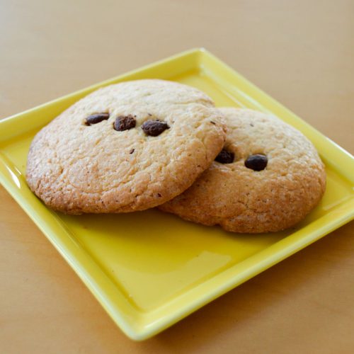 Two gluten-free chocolate chip cookies on a yellow plate