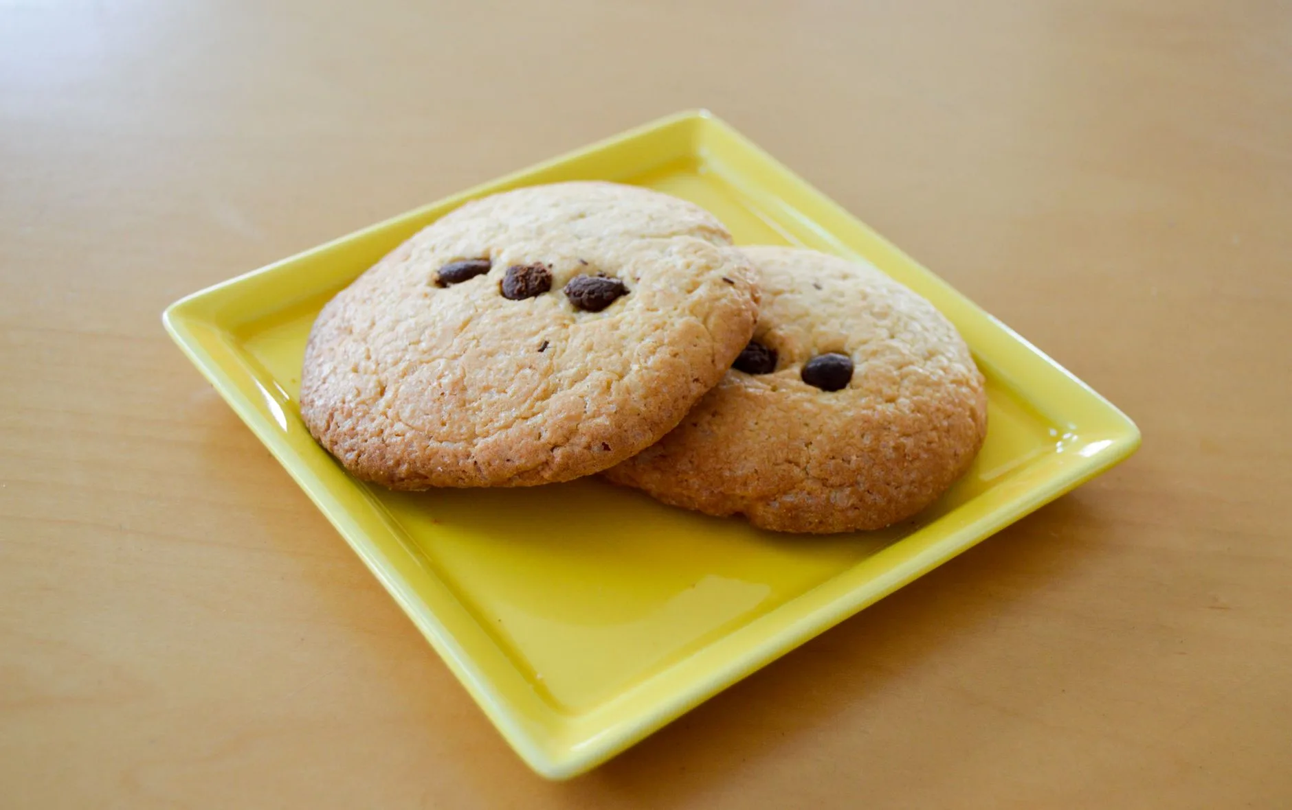 Two gluten-free chocolate chip cookies on a yellow plate