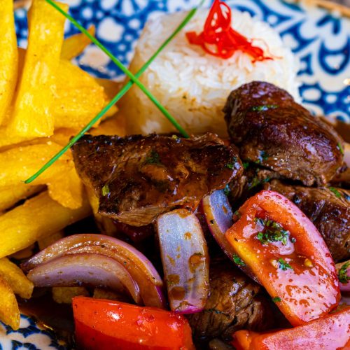 Peruvian lomo saltado with steak, fries, onions, and tomatoes served over rice in a bowl