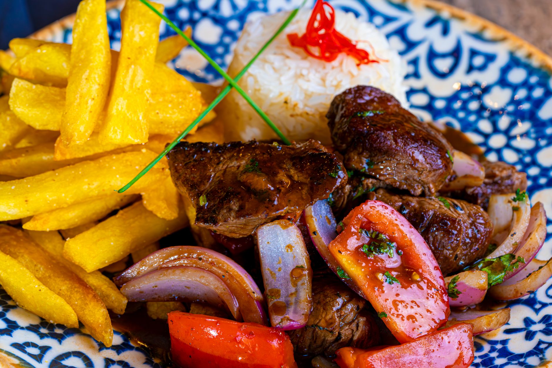 Peruvian lomo saltado with steak, fries, onions, and tomatoes served over rice in a bowl