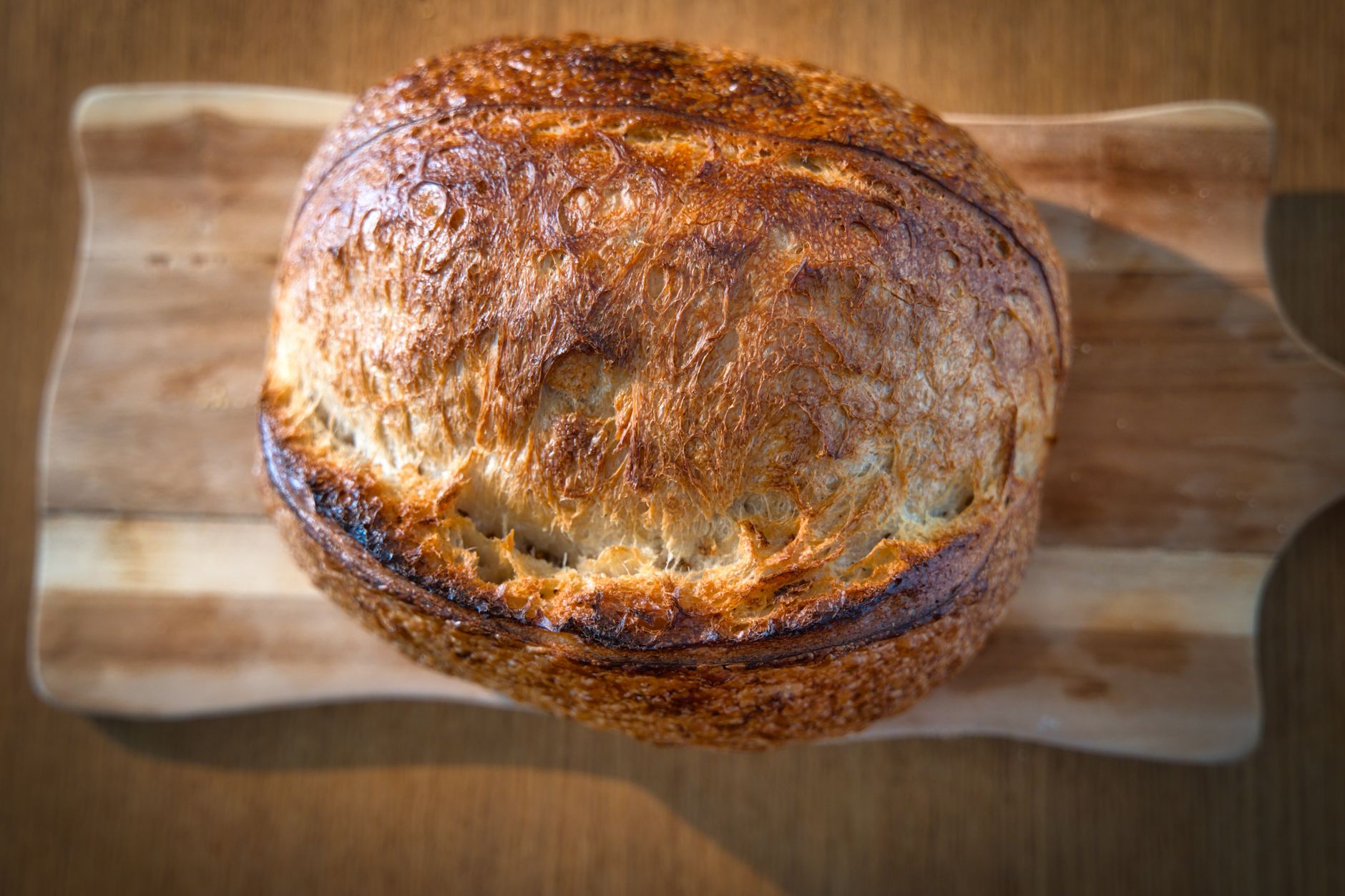 Crusty homemade sourdough bread loaf on a wooden board, sliced to show open crumb