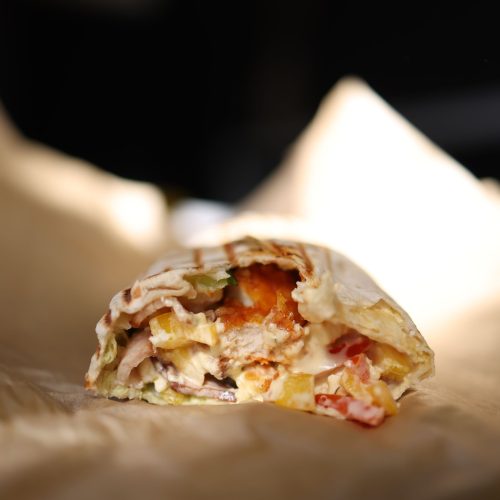 Doner kebab wrap cut open to show sliced meat and vegetables, on paper