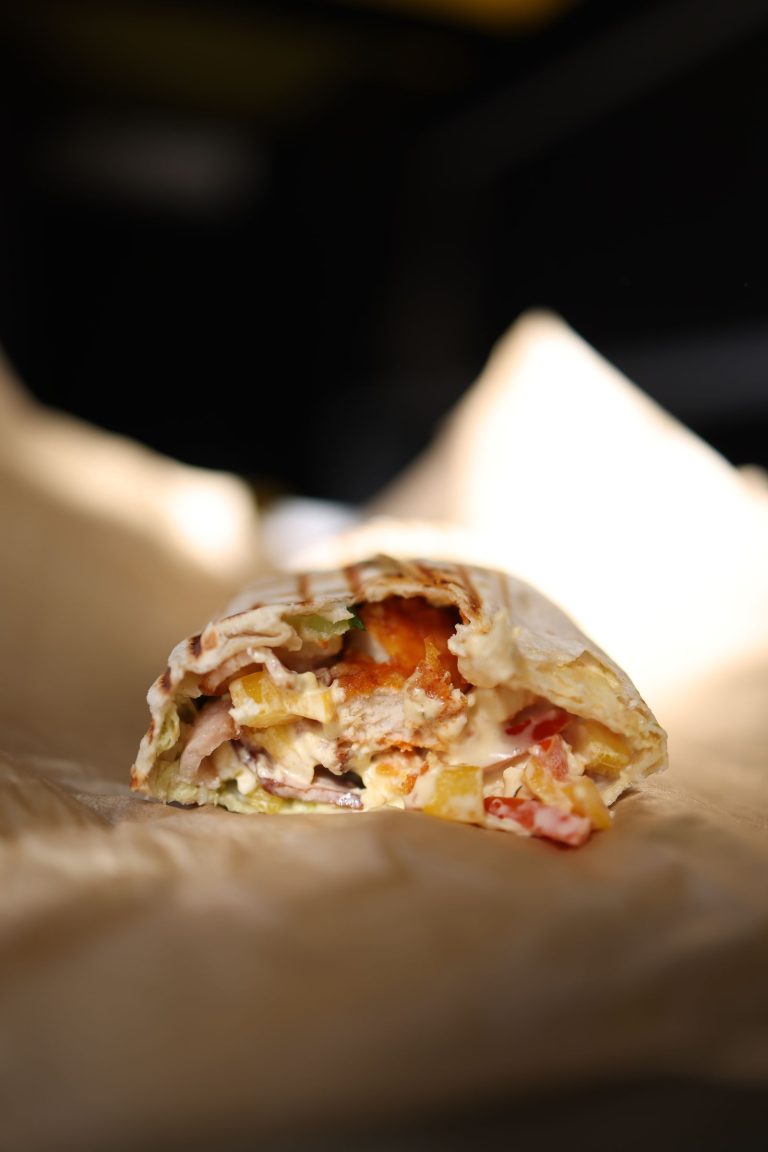 Doner kebab wrap cut open to show sliced meat and vegetables, on paper