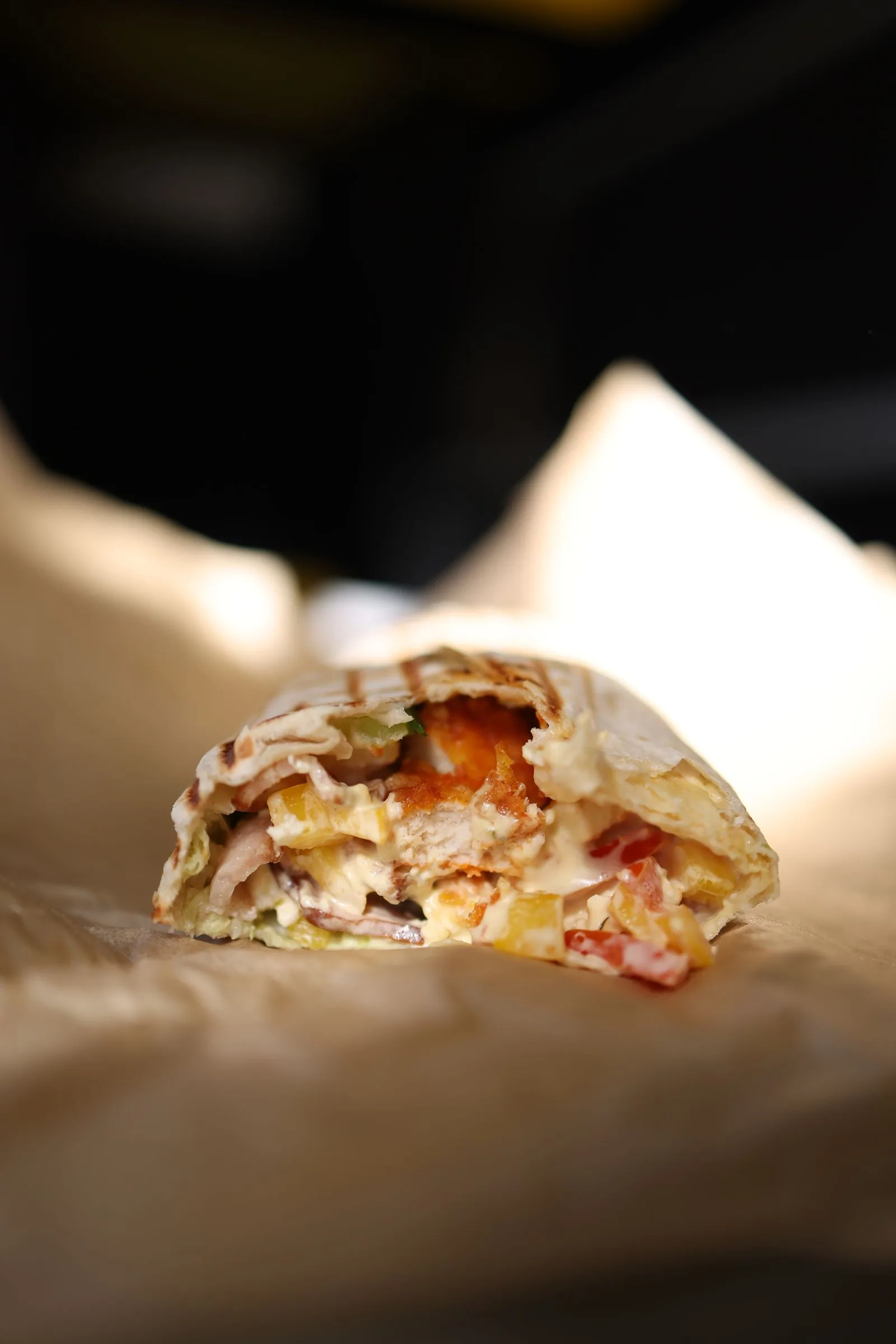 Doner kebab wrap cut open to show sliced meat and vegetables, on paper