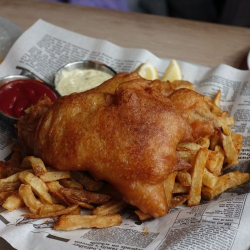 Battered fish and chips served on newspaper with lemon, ketchup and tartare sauce