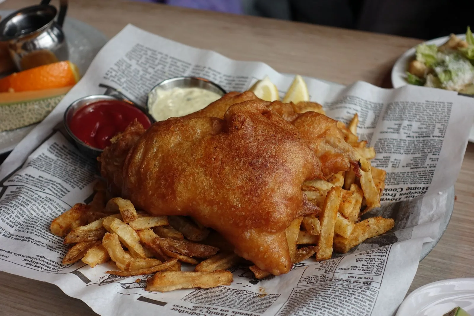 Battered fish and chips served on newspaper with lemon, ketchup and tartare sauce