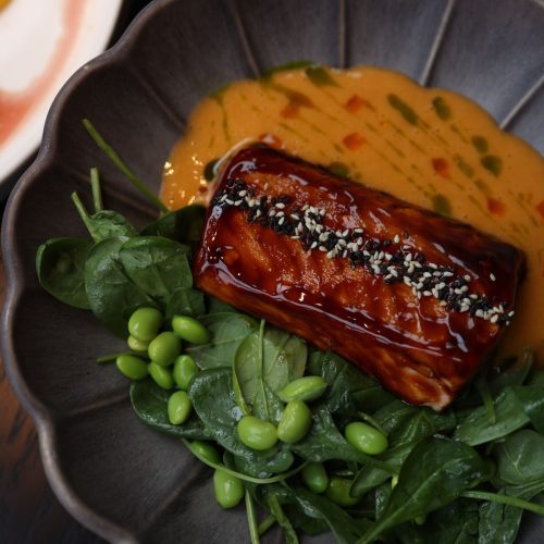 Glossy honey miso glazed salmon topped with sesame seeds on spinach and edamame