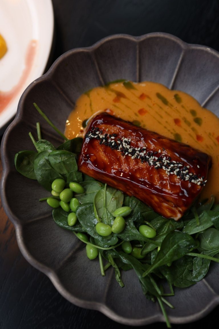 Glossy honey miso glazed salmon topped with sesame seeds on spinach and edamame