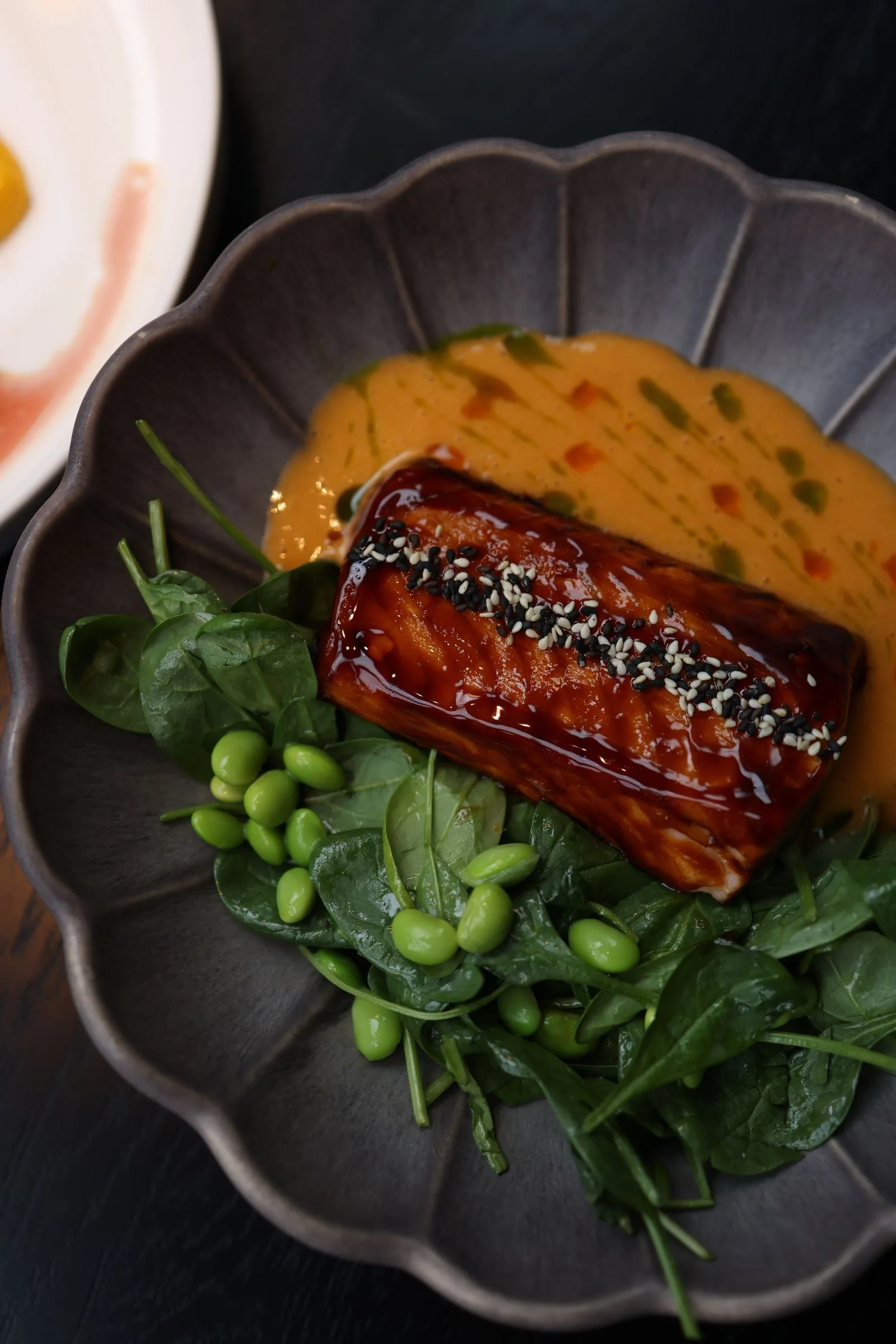 Glossy honey miso glazed salmon topped with sesame seeds on spinach and edamame