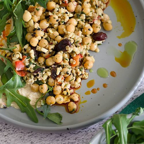 Delicious Mediterranean salad with chickpeas, hummus, arugula, and olives, drizzled with olive oil.
